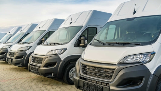 Row of white commercial vans parked in a lot under a clear sky.