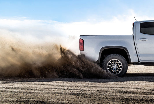 pickup truck spinning rear tire and kicking up dirt and dust